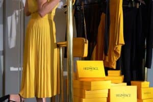 Eine gelb gekleidete Frau fährt auf einem hotel Gepäckwagen mit gelben schachteln darauf