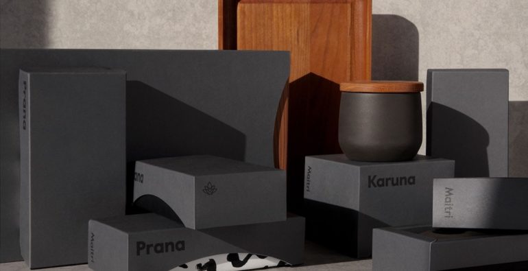Elegante Packagings aus schwarzem Karton. Auf einem der Kartons steht ein kleines schwarzes Gefäß mit einem Deckel aus einem mitteldunklen Holz. 
