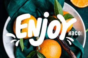 Das Logo der Genuss-Plattform Enjoy, das weiß und bold auf dem Foto von Orangen zu sehen ist, die mit einem Messer in einer Schüssel liegen