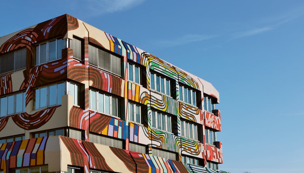 Mit bunten Wax-Print-Mustern überzogene Hausfassade des Stoffherstellers Vlisco, gestaltet von Simone Post, obere Ecke mit blauem himmel