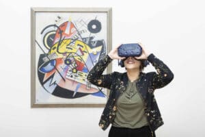 Frau mit VR Brille im Hintergrund das Kandinsky Gemälde weißer Punkt