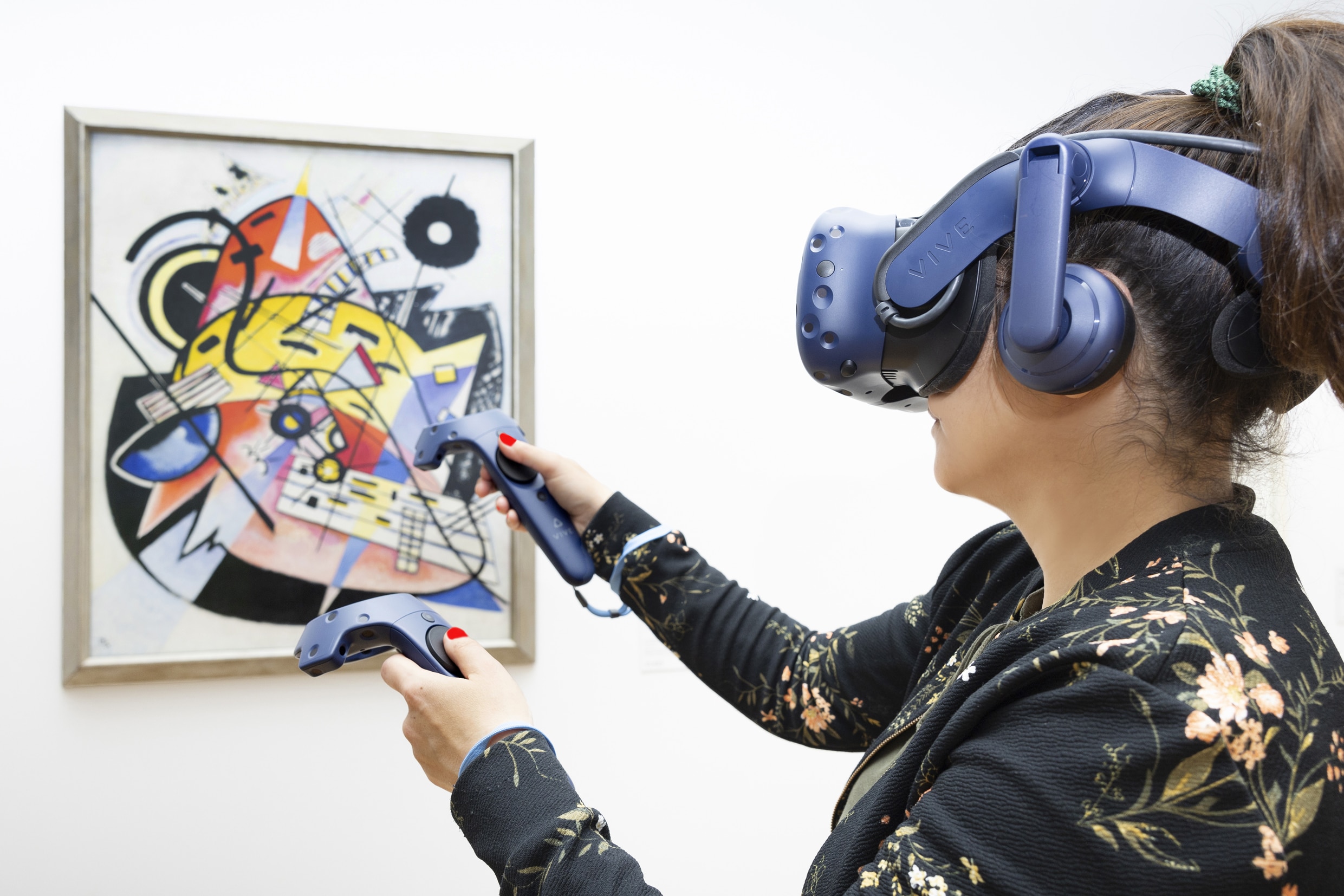 Gemälde Weißer Punkt von Kandinsky im Hintergrund und Frau mit VR-Headset und Controllern im Vordergund