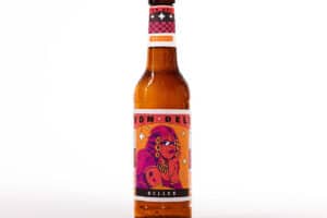 Eine Bierflasche mit Label in waremn Farbtönen vor weißem Grund. Die Illustration zeigt eine mürrisch dreinblickende Dame in knalligem pink