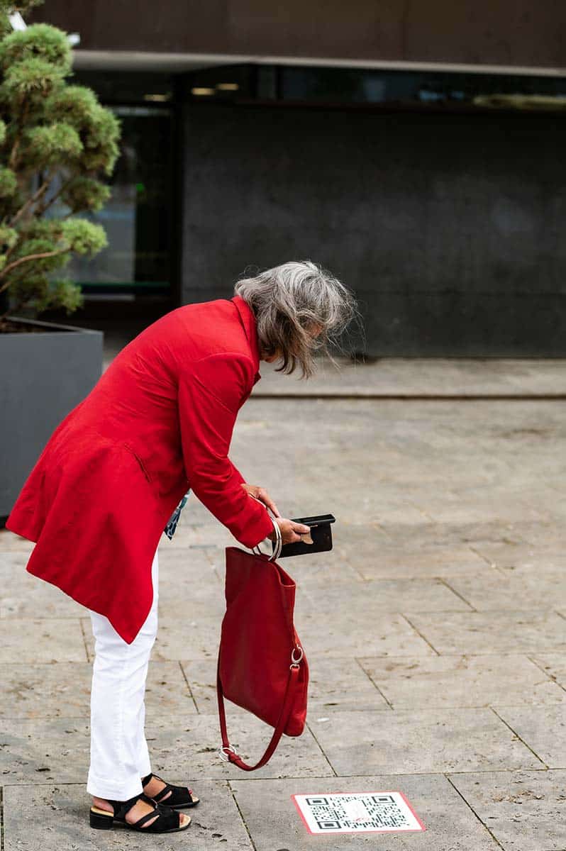 Eine Frau in Rot gekleidet scannt einen Qr Code am Boden
