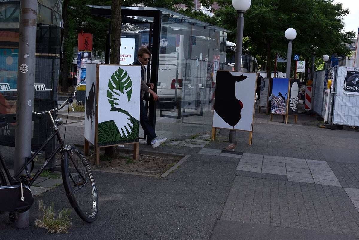 Plakate um eine Bushaltestelle herum, mit denen Passanten interagieren