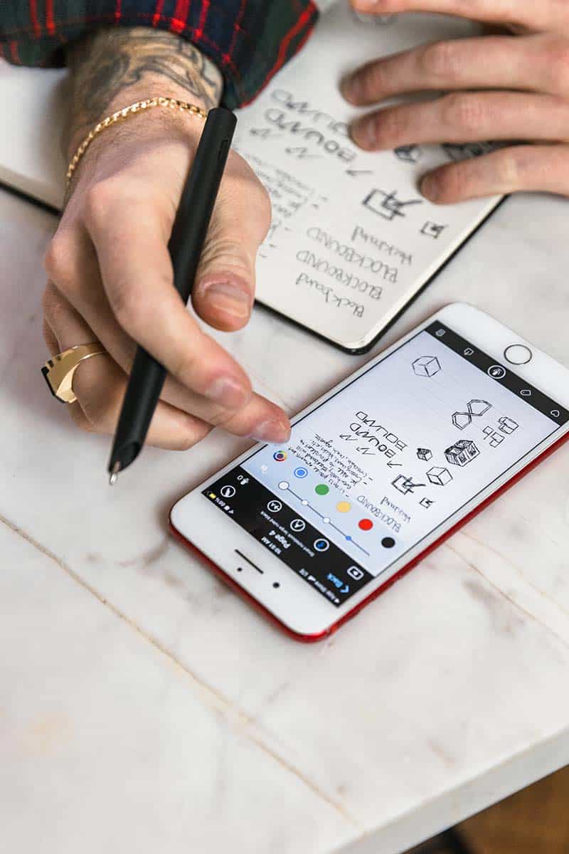Zwei Hände zeichnen in einem Notizbuch und bedienen parallel die molekine smart note app