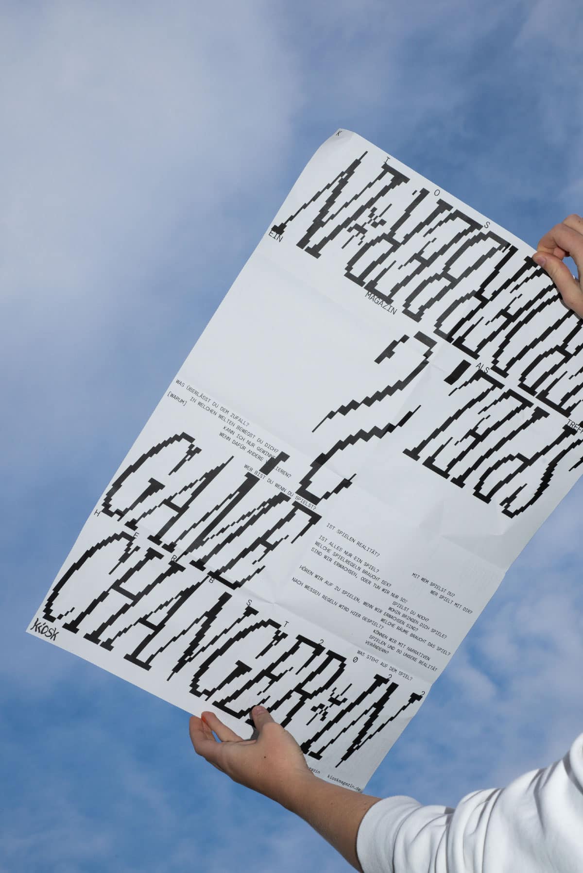 Ein weißes poster mit pixelig verzogener Schrift wird in den blauen Himmel gehalten