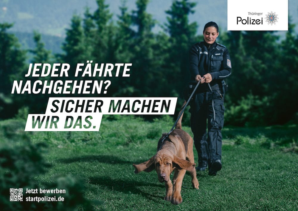 Recruitingkampagne für die Thüringer Polizei: Beamtin mit Spürhund in wäldlichem Gebiet. Zu lesen: »Jeder Fährte nachgehen? Sicher machen wir das.«