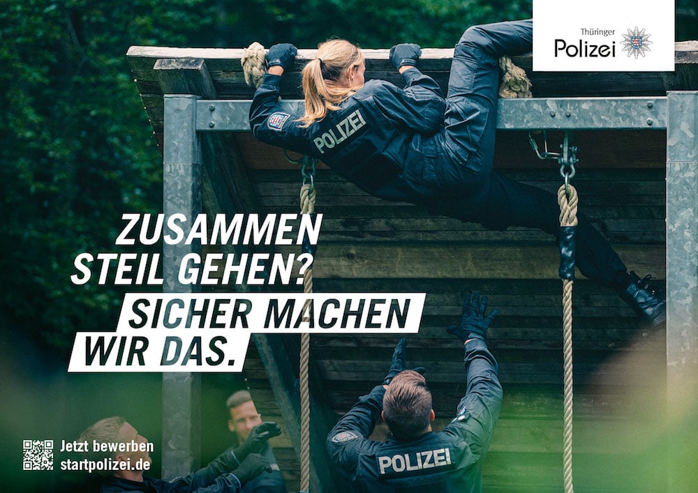 Recruitingkampagne für die Thüringer Polizei: Beamt:innen bei einem Hindernisparcours. Eine Person erklettert ein hohes Hindernis. Zu lesen: »Zusammen steil gehen? Sicher machen wir das.«