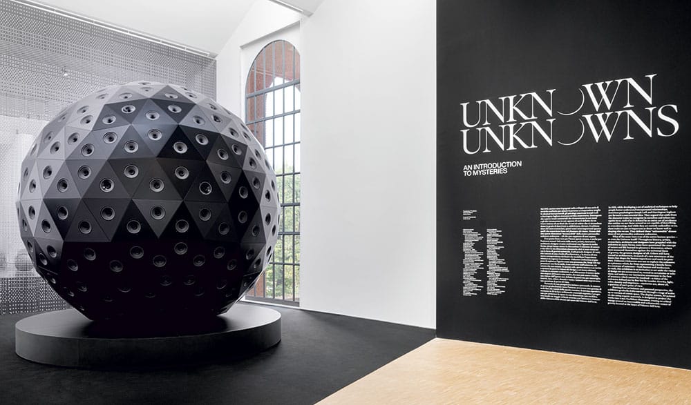 An installation by Yuri Suzuki called »Sound of the Earth. Chapter 3«. A huge black globe is exhibited in a modern gallery. The globe is constructed of sound speakers that let the audience hear collective soundscapes according to their geographic position.