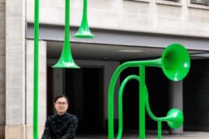Yuri Suziki sitzt mit knallgrüner Soundskulptur mit großen Tröten vor Wohnhaus