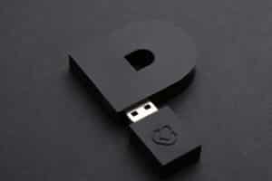 Ein schwarzer USB Stick in form eines Ps liegt auf schwarzem Grund