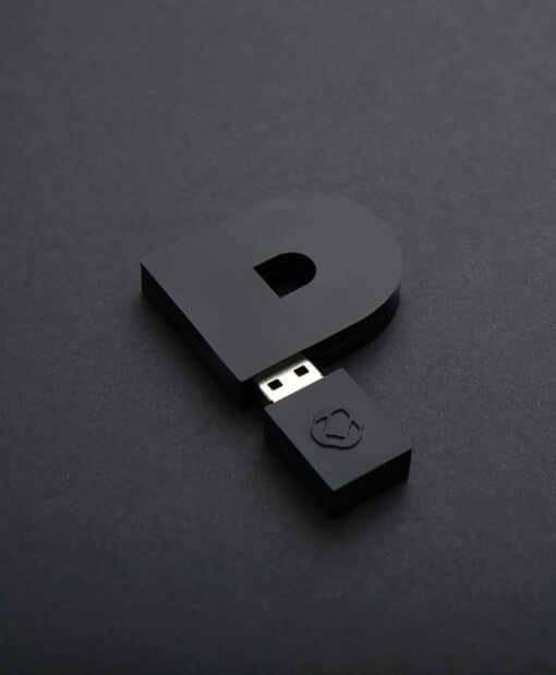 Ein schwarzer USB Stick in form eines Ps liegt auf schwarzem Grund