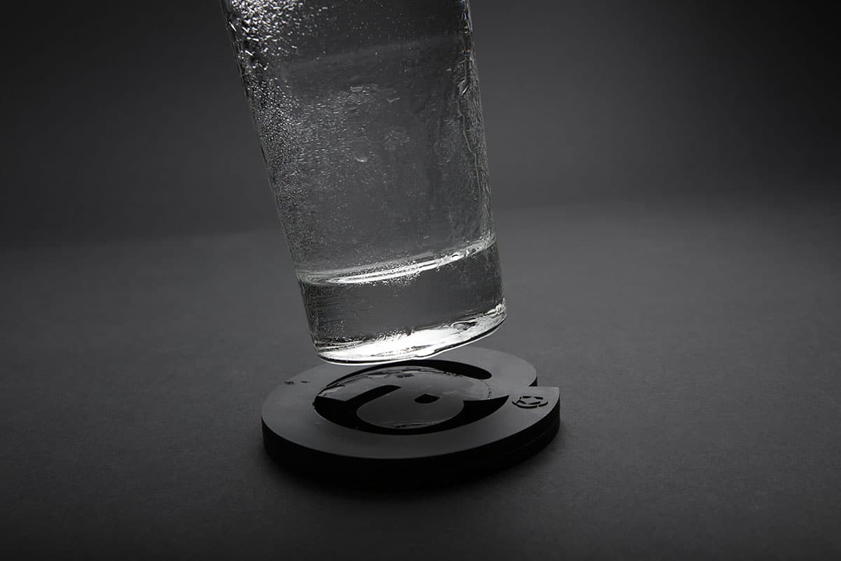 Ein Wasserglas scheint über einem Untersetzer zu schweben, der wie ein schwarzes @ Zeichen geformt ist
