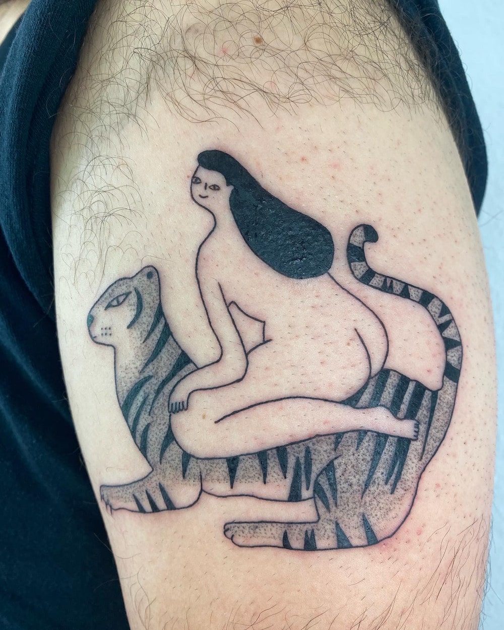Tattoo auf einem behaarten Oberarm. Das Motiv ist eine nackte Frau mit schwarzen Haaren, die auf einem Tiger sitzt und lächelt