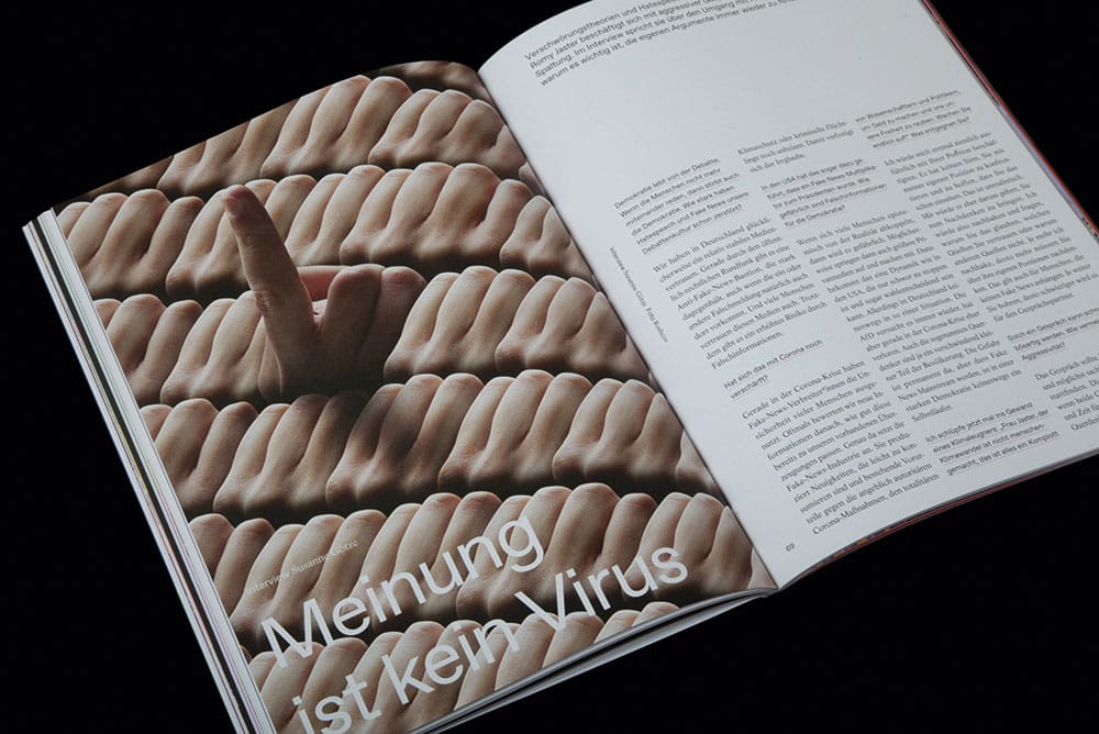 Doppelseite aus dem "Albert"-Kundenmagazin mit dem Foto von vielen Händen, von denen nur eine sich meldet, auf der linken Seite und einem Text auf der rechten Seite. Vor dem Foto steht die Headline des Textes "Meinung ist kein Virus"