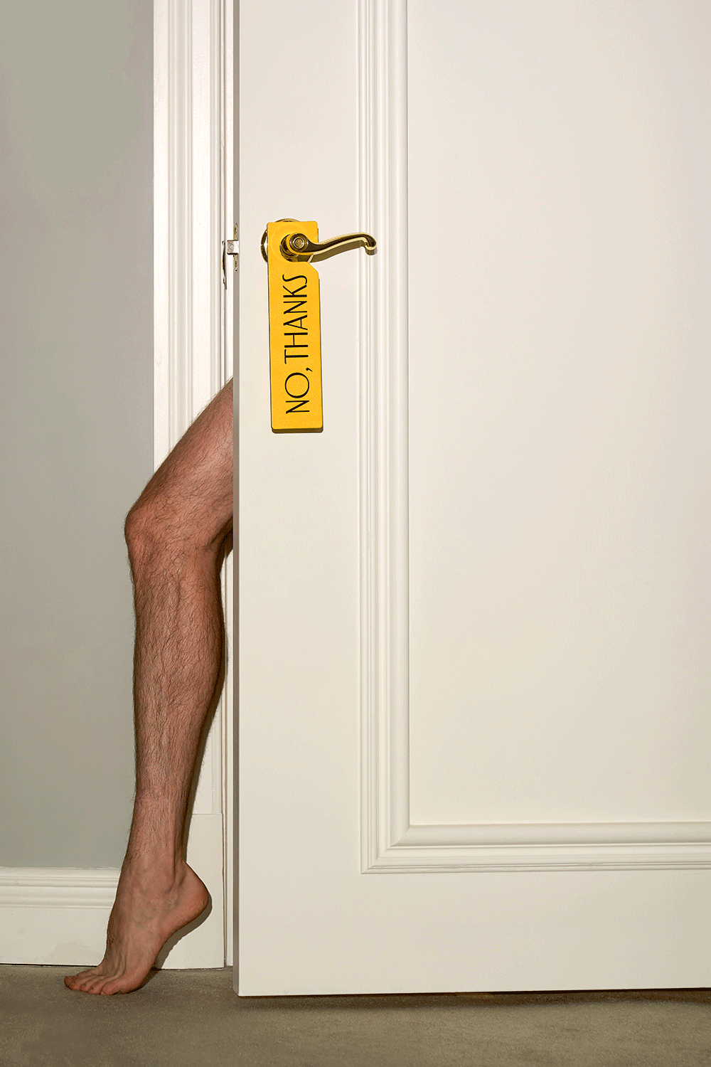 Hotelbranding: Ein stark behaartes Bein schaut hinter einer Hoteltür hervor, an deren Klinke ein gelbes Schild hängt auf der "No, Thanks" geschrieben ist
