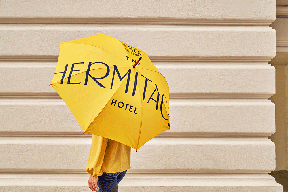 Hotelbranding: Person mit knallgelben Hermitage-Regenschirm