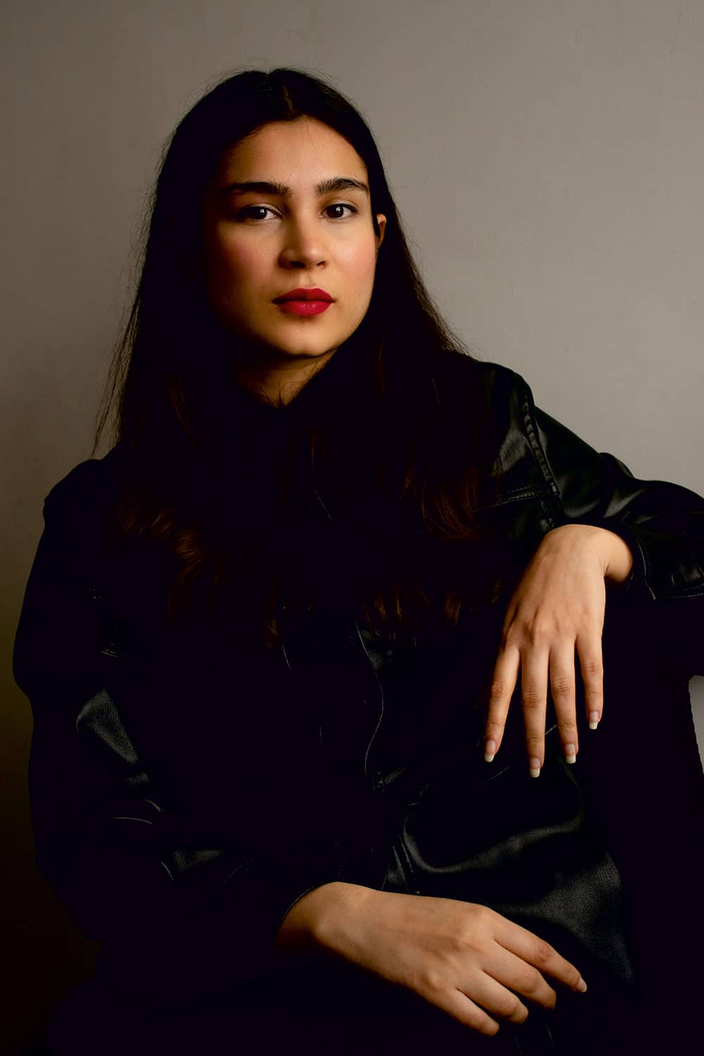 Portrait of Khyati Trehan in black shiny clothes and dark straight hair, wearing red lipstick. She is looking into the camera.