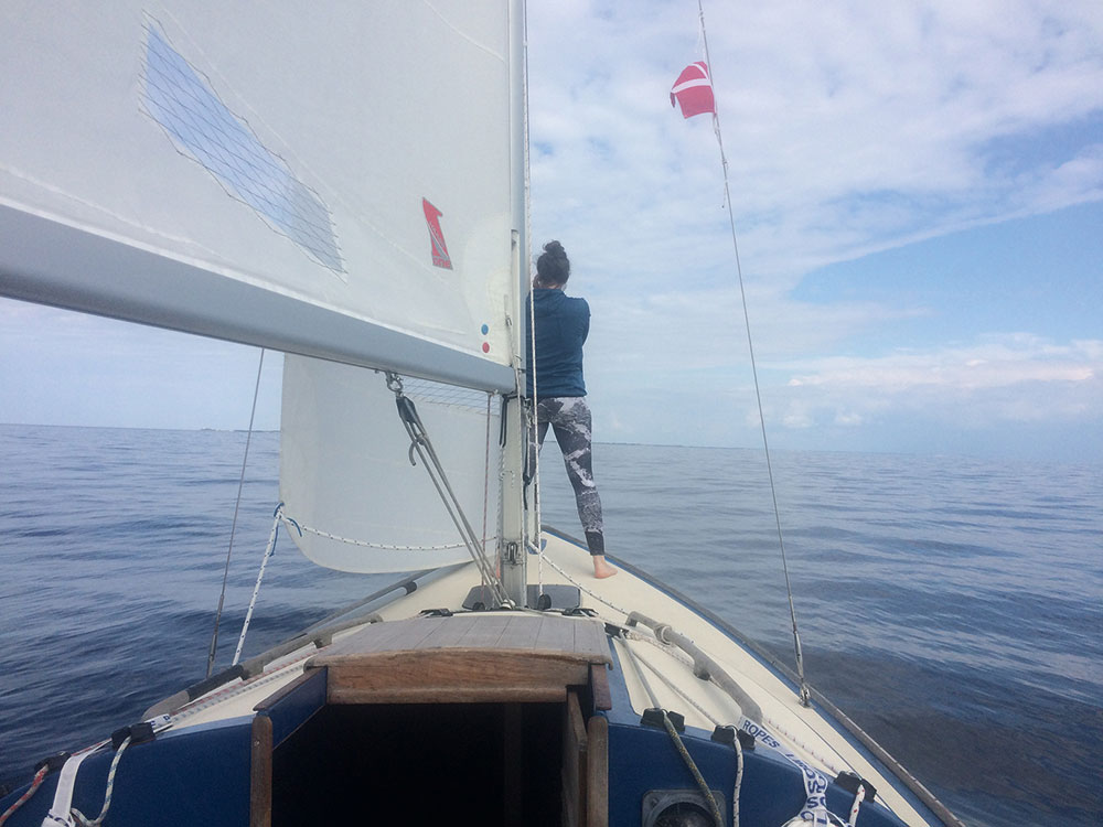 Ann Eckert steht an der Spitze eines Segelbootes und schaut aufs Meer und die Wolken