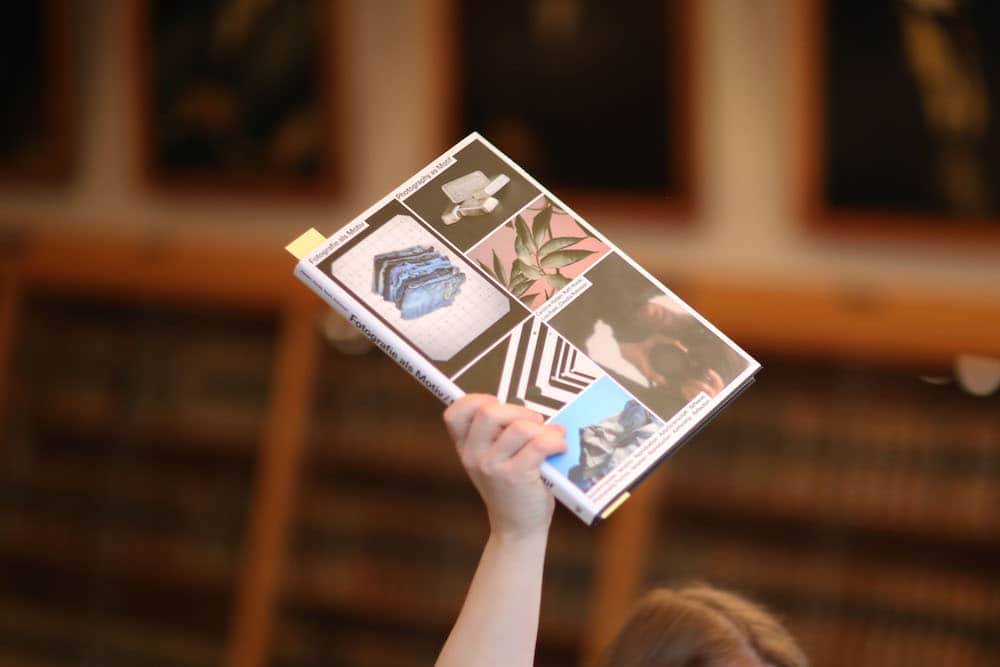 Das sind die schönsten Bücher aus aller Welt 2023. Eine Hand hebt das Gewinner:innenbuch »Fotografie als Motiv« in die Höhe