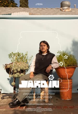 Eine Person sitzt vor einer blauen Wand mit bepflanzten Gefäßen und schaut in die Kamera. Mit weißer Schrift wird das Parfum Jardin beworben.
