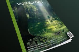 Das Cover der Wanderlust zeigt einen Serifenschriftzug über einem Wanderer im Wald. Über Rücken und Seite des Covers zieht sich ein stilisierter Gurt
