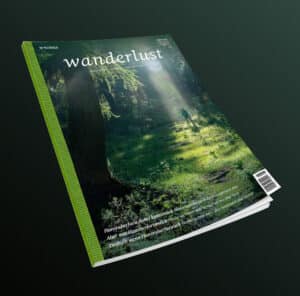 Das Cover der Wanderlust zeigt einen Serifenschriftzug über einem Wanderer im Wald. Über Rücken und Seite des Covers zieht sich ein stilisierter Gurt