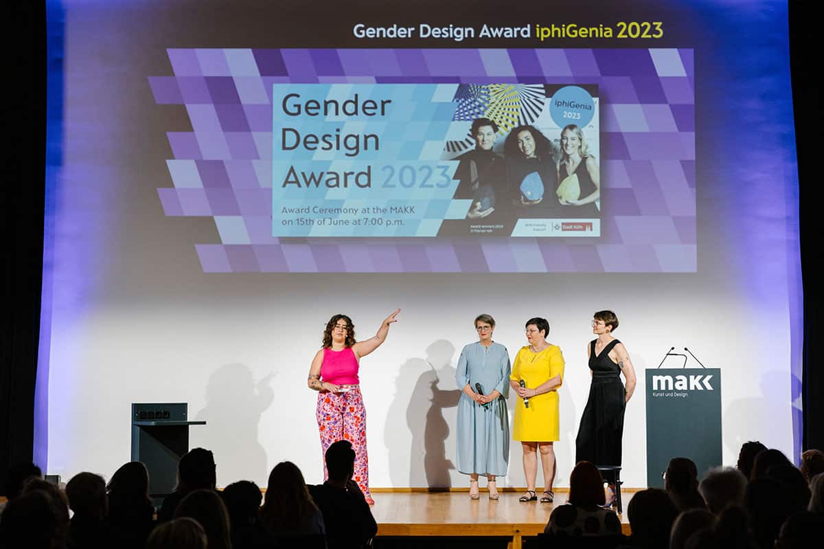 Vier bunt gekleidete Menschen stehen auf einer Bühne unter dem Banner des Gender Design Awards