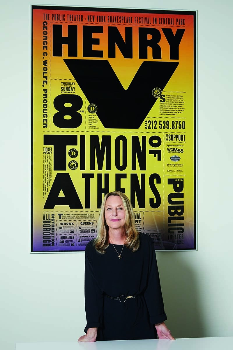 Paula Scher steht vor einem gelben typografisch gestalteten Poster