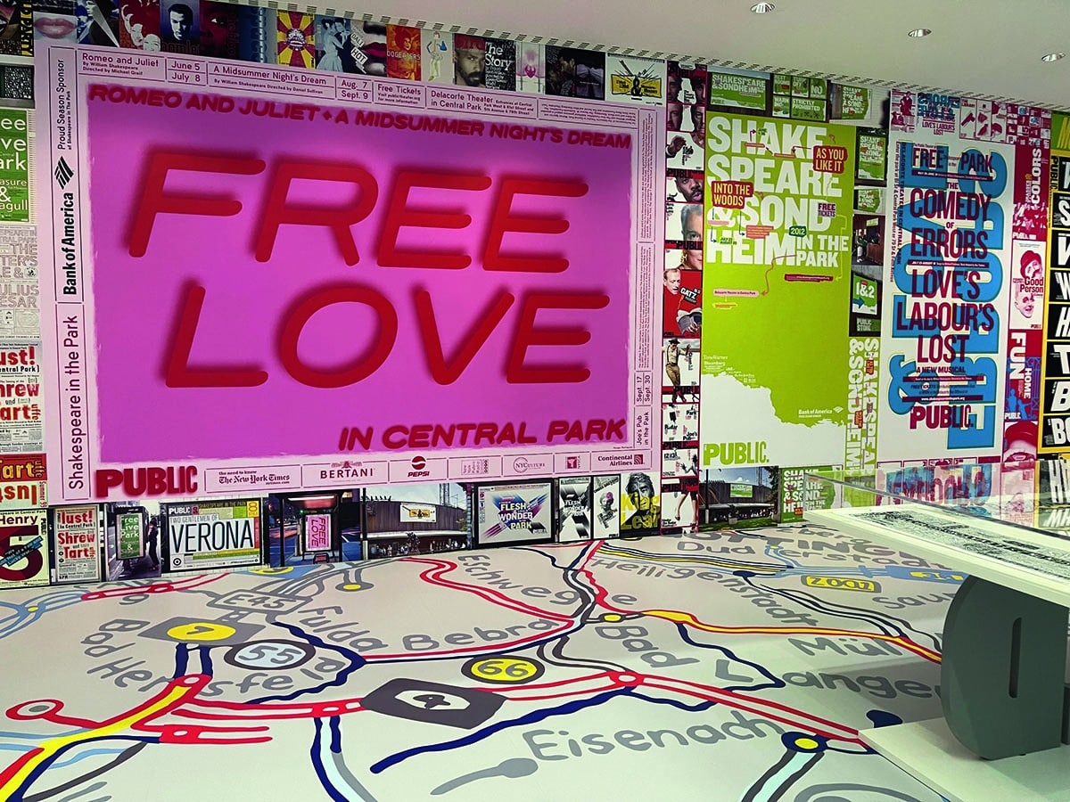 Ein Ausstellungsraum, der komplett mit Schrift ausgekleidet ist. An der wand hängt ein rosa Plakat mit dem Aufdruck »free love«