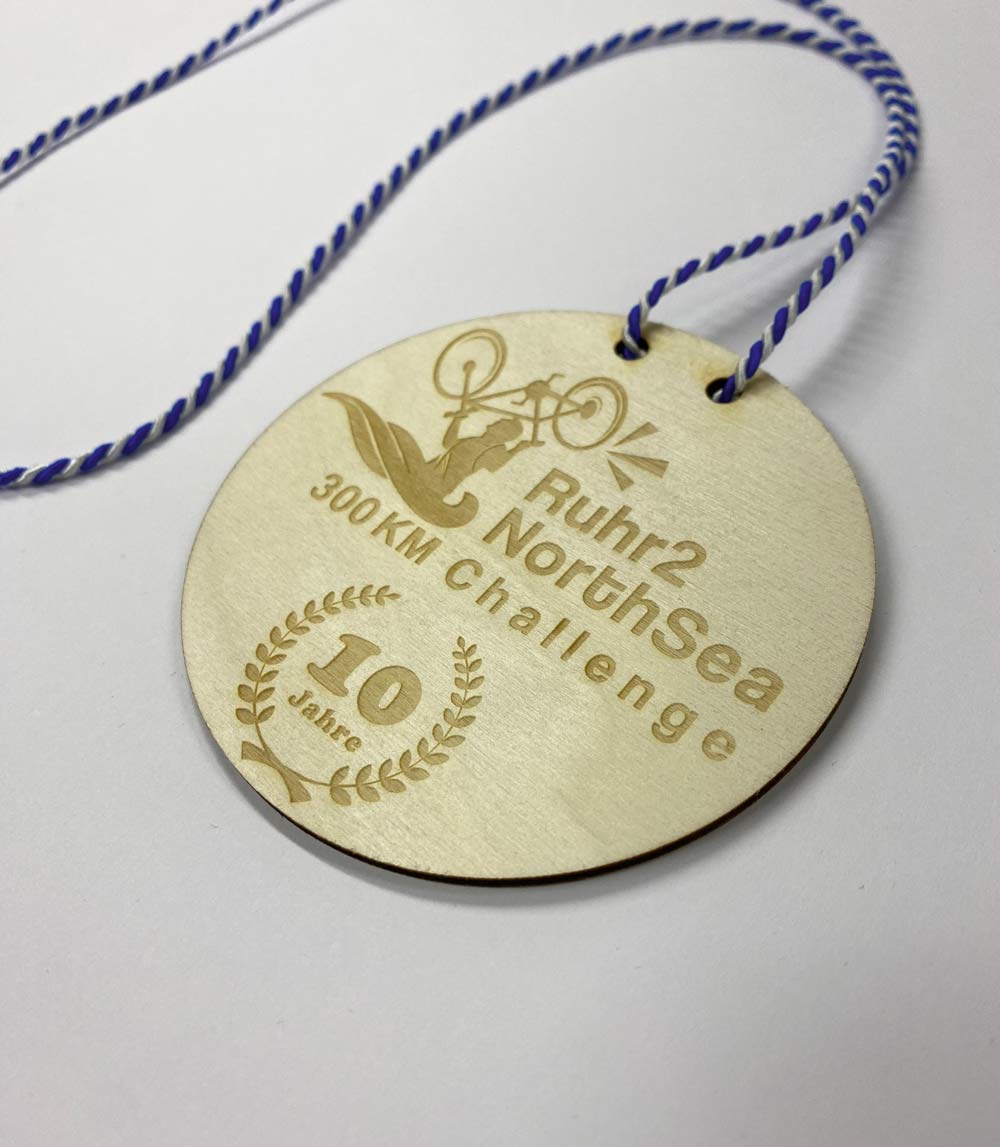 Bei dieser Medaille aus Holz, die WOWI auf der Rückseite vierfarbig bedruckte, sind die sichtbaren Schmauch­ spuren ein gewolltes Gestaltungselement