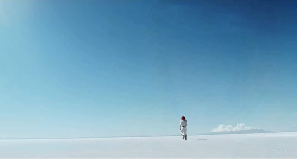 Screenshot Sora OpenAI Person in Raumanzug auf Planetenoberfläche. Wolken im Hintergrund, blauer Himmel.