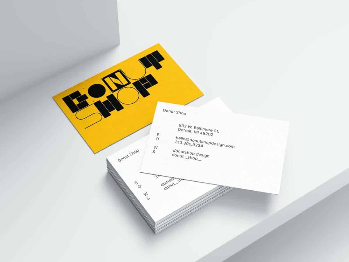 Ein Stapel von Visitenkarten mit einem modernen Design auf einer hellen Oberfläche. Eine Karte oben ist gelb mit schwarzen Buchstaben, die 'FORUM SHOP' lesen, und untere Karten zeigen Kontaktinformationen wie Adresse, E-Mail und Telefonnummer auf weißem Hintergrund
