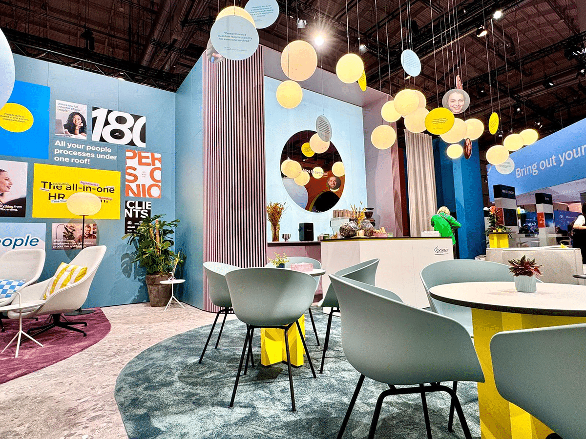 Detailansicht eines Messestands mit großen gelben und blauen Werbetafeln und dekorativen grünen Elementen