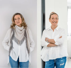 Sabine Kraus und Katharina Kraus stehen nebeneinander, beide tragen weiße Hemden und blaue Jeans. Sabine trägt zusätzlich einen grauen Fransenschal. Beide lächeln in die Kamera.