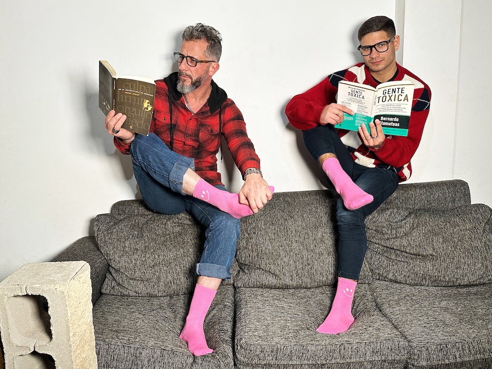 Zwei Männer auf der Couch mit rosa Socken an und Büchern in der Hand