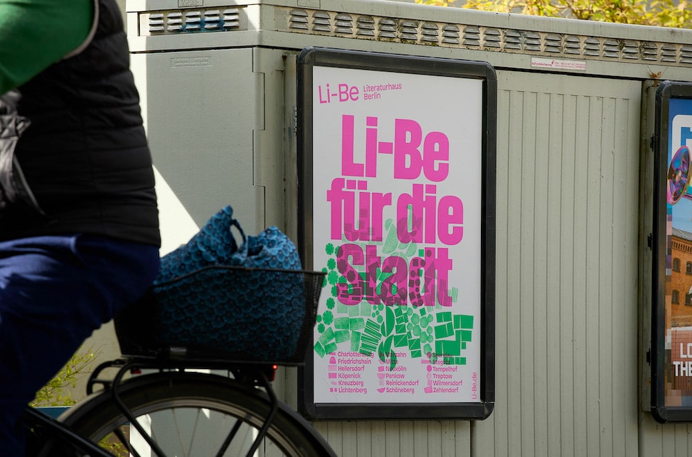 Pink und grünes Plakat für Li-Be für die Stadt, das an Stromkasten hängt und Fahrradfahrerin fährt vorbei