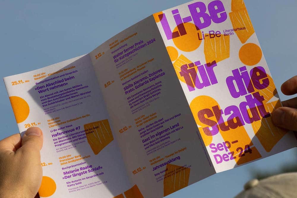 Zwei Hände halten Flyer für "Li-Be für die Stadt", der in orange und lila leuchtet