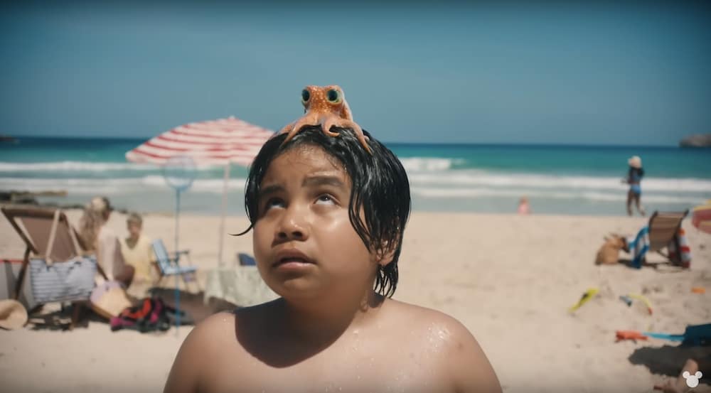 Junge am Strand hat einen kleinen orangenen Oktopus auf dem Kopf