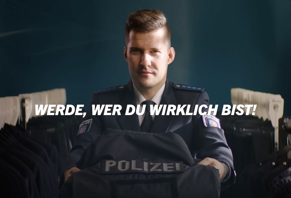 Junger Polizist hält einem eine ordentlich gefaltete Polizeiuniform entgegen zu dem Slogan: Werde, wer du wirklich bist!