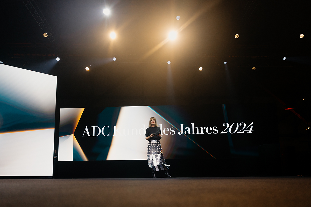 Frau auf großer Bühne unter Scheinwerferlicht, vor einem LED-Display mit der Aufschrift „ADC Kunde des Jahres 2024“ bei einer Preisverleihung.