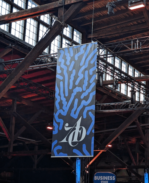 Großes vertikales Banner mit blau-schwarzem Muster und ADC-Logo hängt in einer Industriehalle.