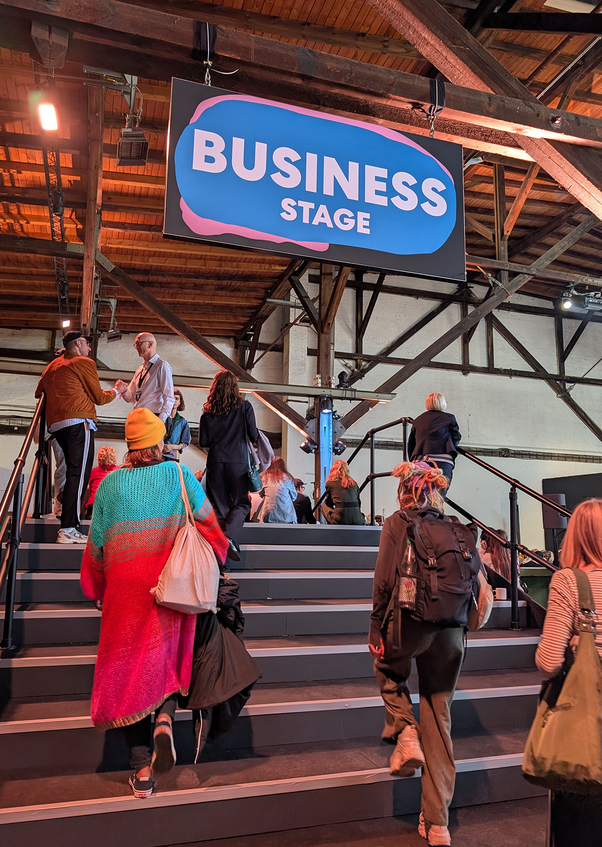 Besucherinnen und Besucher steigen eine Treppe zur „Business Stage“ hinauf; darüber hängt ein großes Schild mit dem Bühnennamen.