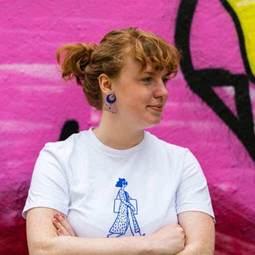 Jessica Rinne trägt kurze Zöpfe, ein weißes T Shirt und posiert mit verschränkten armen vor einer pinken Wand