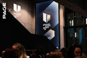 Menschen auf einer Abendveranstaltung, im Hintergrund leuchtet ein großes Display mit dem Logo des german brand award 26