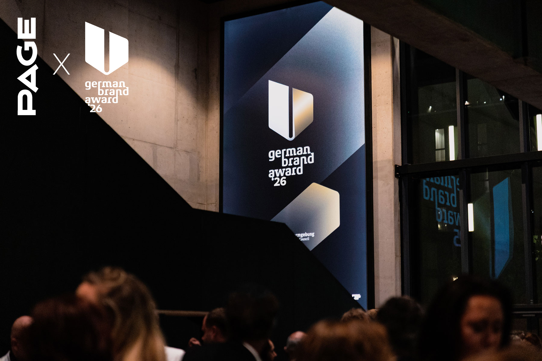 Menschen auf einer Abendveranstaltung, im Hintergrund leuchtet ein großes Display mit dem Logo des german brand award 26
