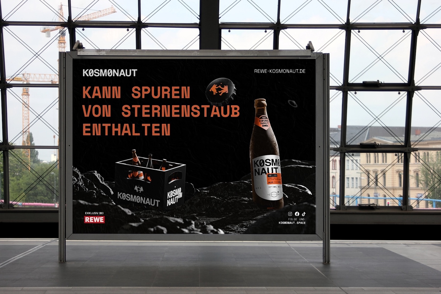 Bahnhofsposter für das Bier „KØSMØNAUT“: Schwarzer, weltraumartiger Hintergrund mit orangefarbener Headline „KANN SPUREN VON STERNENSTAUB ENTHALTEN“, rechts eine Bierflasche, links ein schwarzer Getränkekasten, unten der Hinweis „exklusiv bei REWE“ und Social-Media-Icons.