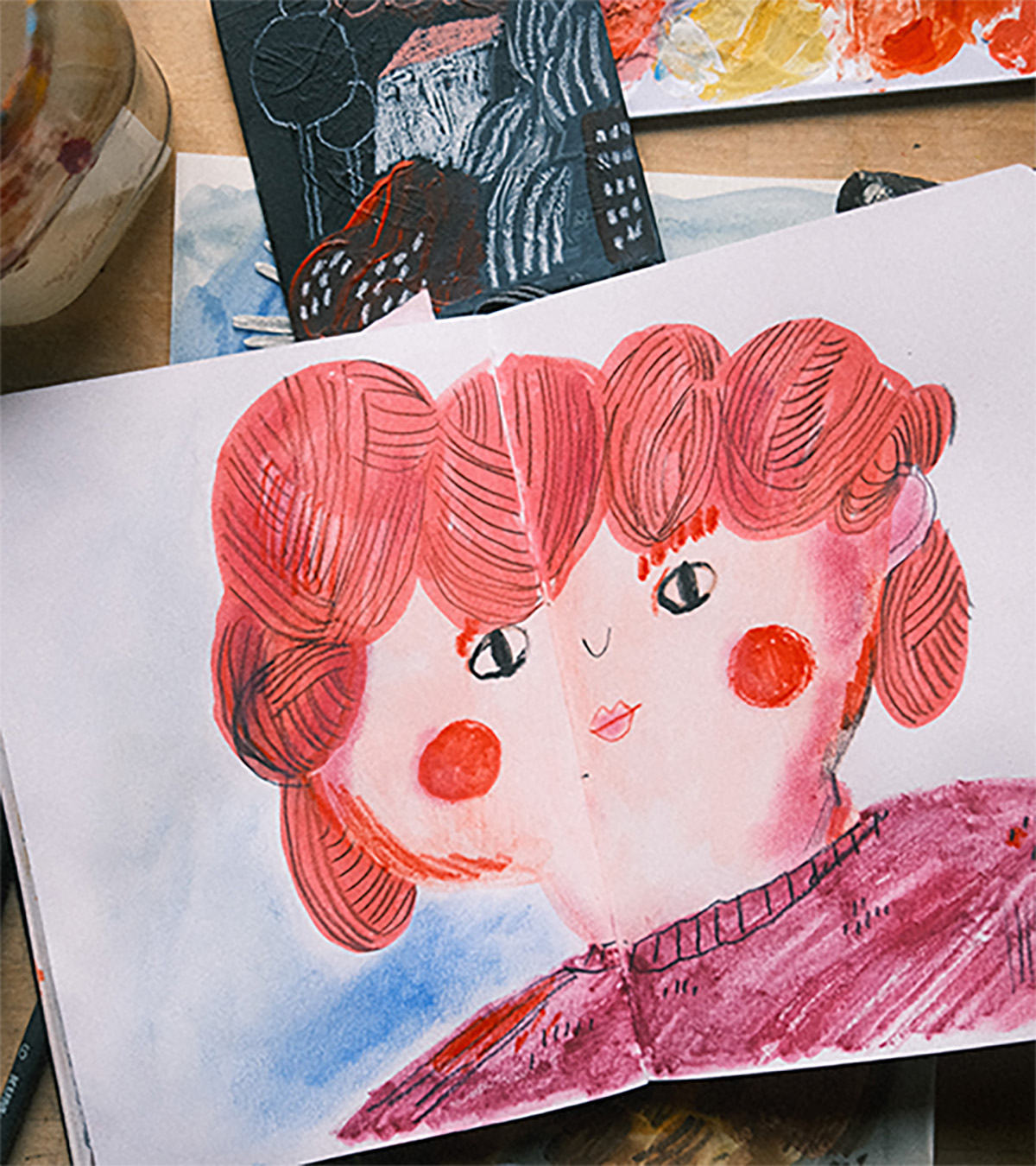 Skurriles Porträt mit doppeltem Gesicht in Rot- und Rosatönen auf einem offenen Skizzenbuch.