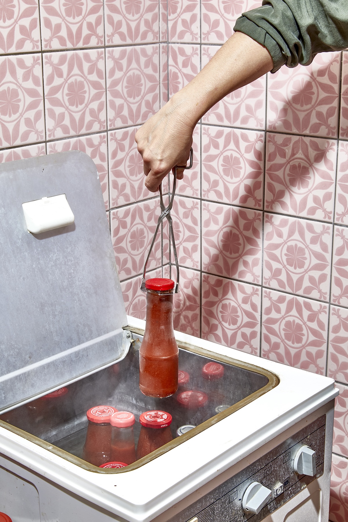 Konservierungsofen vor rosafarben gemusterten Kacheln und mit eingekochenden Tomaten in der Flasche
